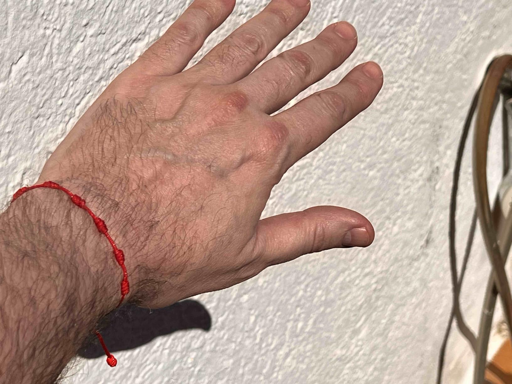 Pulsera roja de los 7 nudos en muñeca junto a pared clara